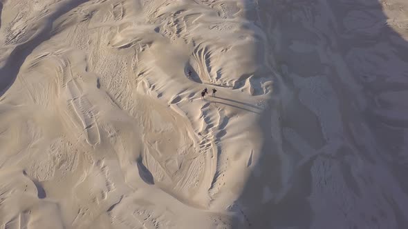 People walking across sand dunes in Newcastle, Australia, aerial follow