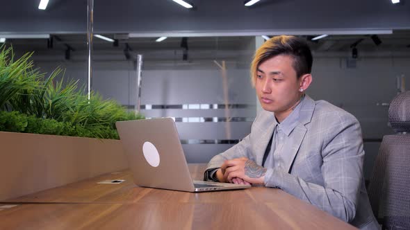 a Young Asian Manager is Working in an Office with a Laptop