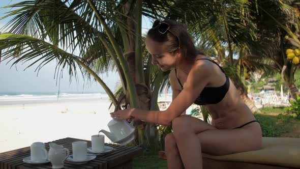 Nice Lady Smiles and Pours Tea in Cup Sitting on Sunbed
