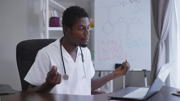 Male African American Scientist Meditating Sitting at Table with Laptop Indoors