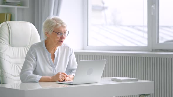 Elegant grey haired mother in glasses greets adult children waving hand