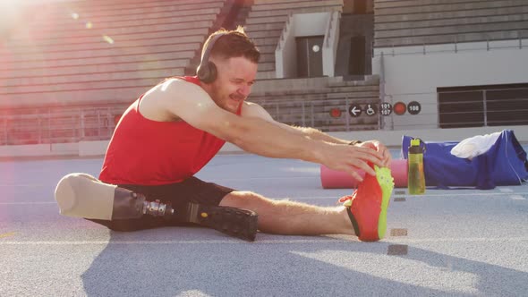 Caucasian disabled male athlete with running blade wearing headphones and stretching