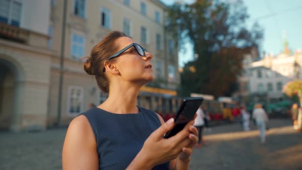 Woman in Glasses Standing on an Old Street, Using Smartphone and Looking Around