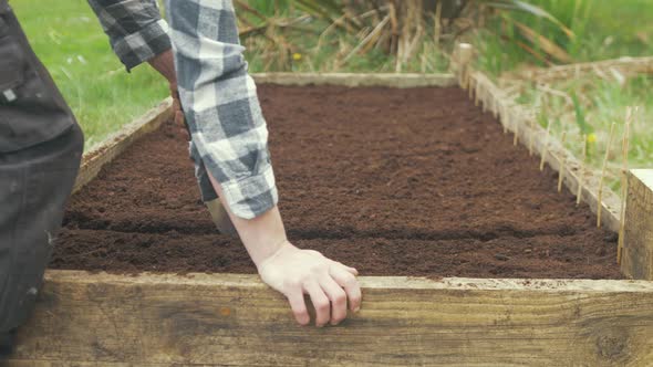 Using trowel making row to sow seeds raised garden bed