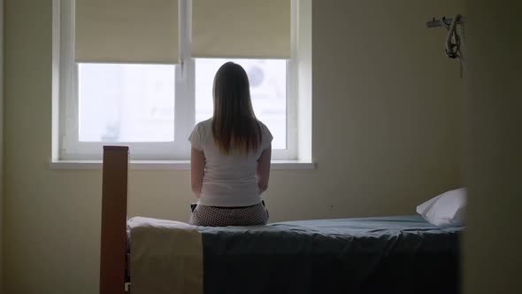 Wide Shot Back View of Young Slim Woman Sitting on Hospital Bed Looking Out the Window