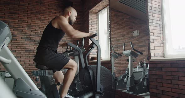 A Young Athlete Does Sports on an Exercise Bike in a Gym