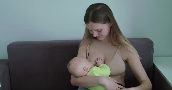 Happy Mother Breastfeeding Her Newborn Baby Admiring Him on Sofa