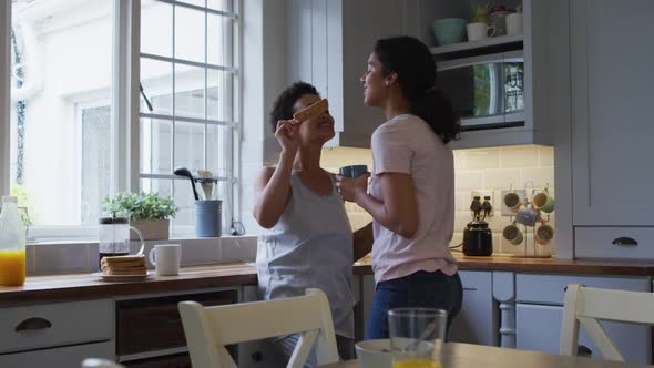 Mixed race lesbian couple hugging and drinking coffee in kitchen