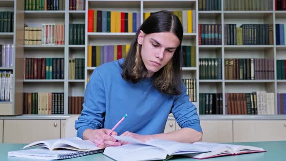 Teenage Guy Studying in College Library Writing in Notebook Reading Books