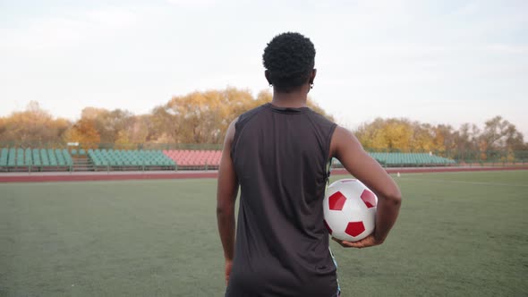 A Young Black Girl Goes on a Soccer Field with a Ball in Her Hand and Turns to the Camera and Smiles