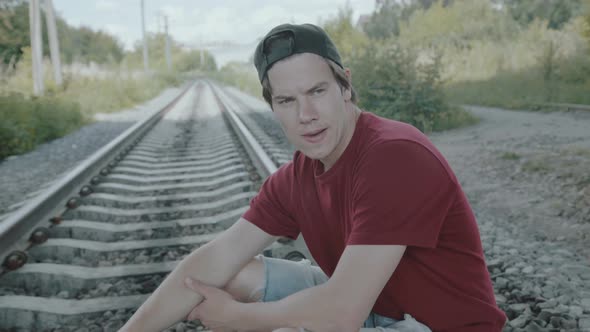 Young Thoughtful Boy Sits on a Rail and Smokes Cigarette