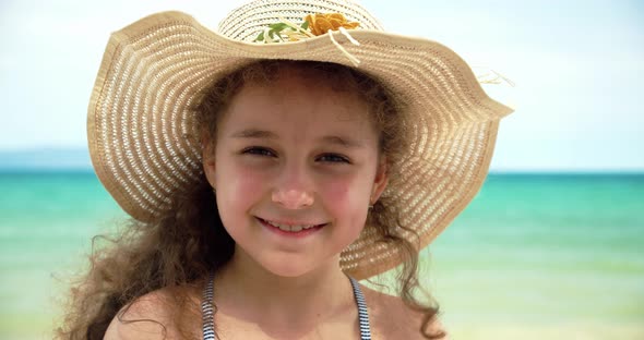 Portrait of a Funny Little Girl in a Hat a Smiling Child Looking at the Camera Stands on the Beach