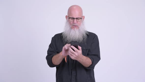 Stressed Mature Bald Bearded Man Using Phone and Getting Bad News