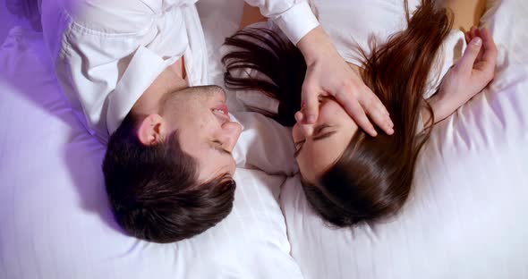 Young Loving Pair Is Lying in Bed at Evening Before Asleep, Talking and Smiling, Man Is Stroking