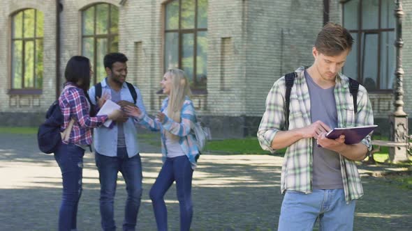 Nerd Male Standing Alone and Reading Essay, Group of Multiracial Friends Talking