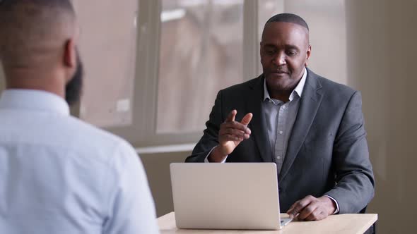 Adult Mature Senior African American Ethnic Businessman Boss Hires Trainee for Work Sitting at Table
