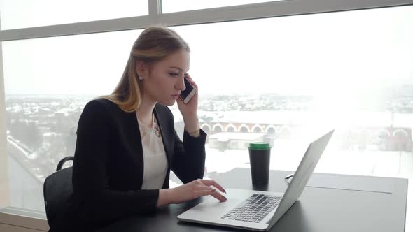 Girl with Laptop Speaks Over Phone at Cafe Table in Winter