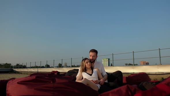 Young Caucasian man and girl are sitting on  roof of a building on soft sofas