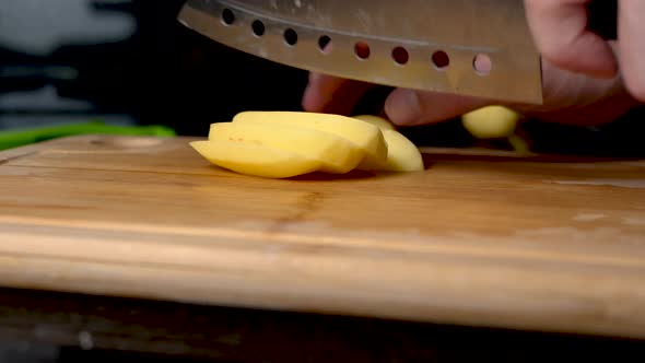 Cutting potatoes on a wooden chopping board with a silver knife. Isolated on black background.