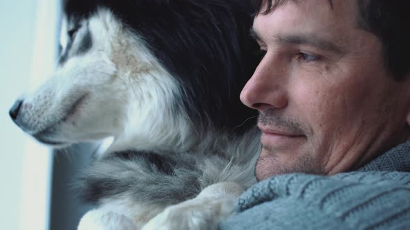 Portrait of Man Holding Husky on Hands Looking Out the Window, Thinking His Thoughts and Dreaming