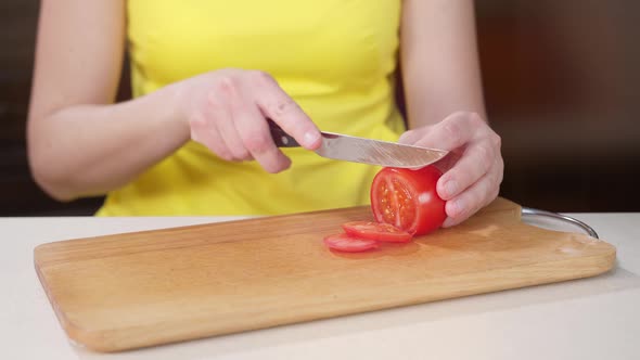 Female Hand of a Cook Cuts a Red Tomato Close Up on a Wooden Board.