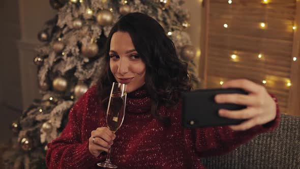 Young Attractive Woman Making Selfie Photo with Sparkling Wine on Christmas Interior Background