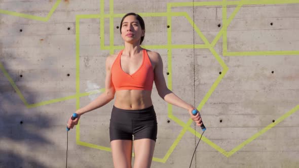 Millennial Hispanic Woman using jump rope in urban park, Medium Shot