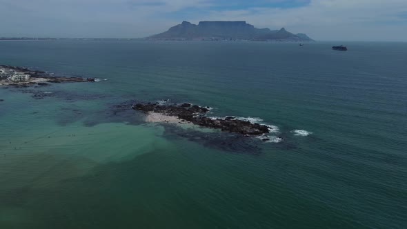 Drone shot of a riff island near Bloubergstrand, Cape Town - drone is circling facing Table Mountain