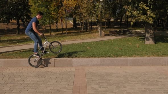 A Young Athletic Guy Rides a BMX Stunt Bike in the Park in the Summer.