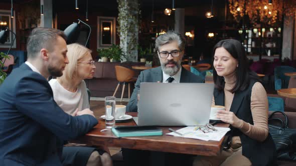 Young and Mature Businesspeople Discussing Project in Restaurant Using Computer at Table