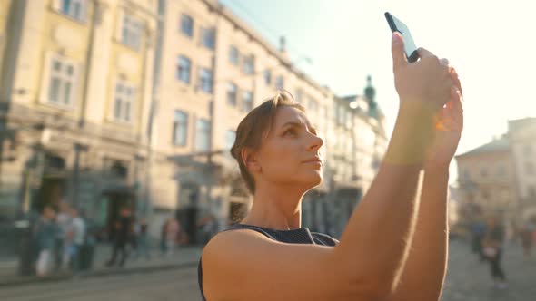 Woman Stands on an Old Street and Takes a Photo or Video on a Smartphone at Sunset