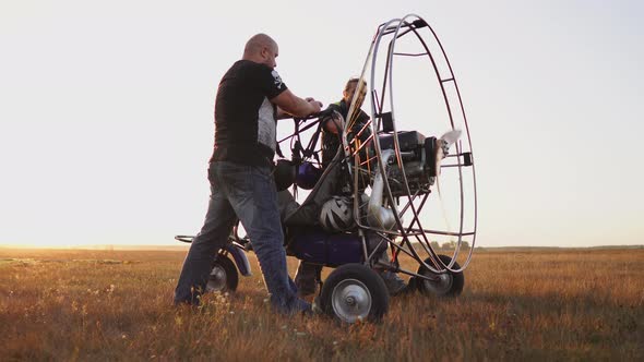 Motor Paraglider Stands in the Field at Sunset with a Wooden Propeller, Two Pilots