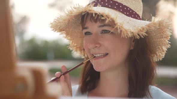 Closeup of Smiling Talented Inspired Woman Thinking Holding Paintbrush in Mouth and Painting in Slow