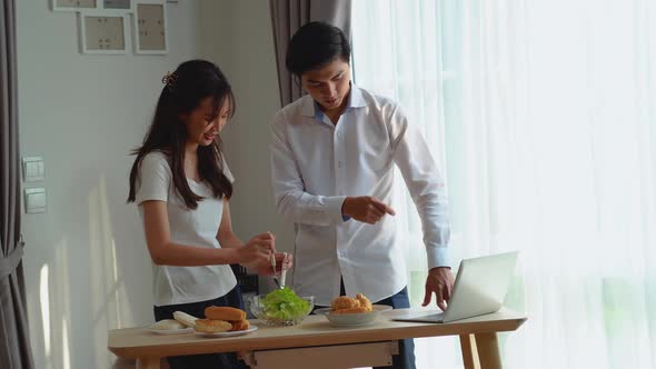 Young Joyful Couple Cooking Healthy Vegetable Salad, Watching tutorial video for recipe on laptop