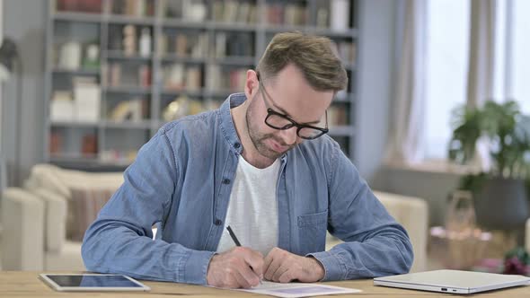 Young Man Thinking and Writing on Paper in Office