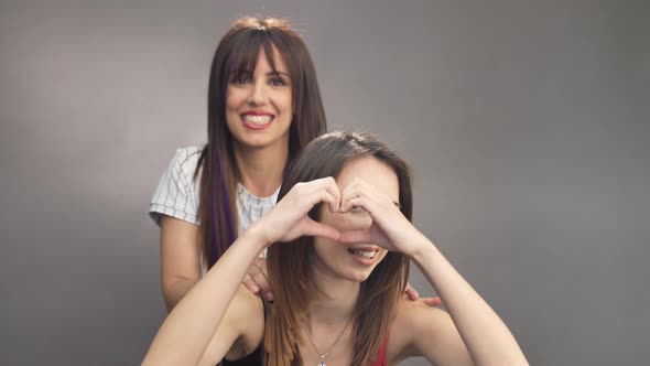 Couple of beautiful women friends posing together making heart symbol with hands