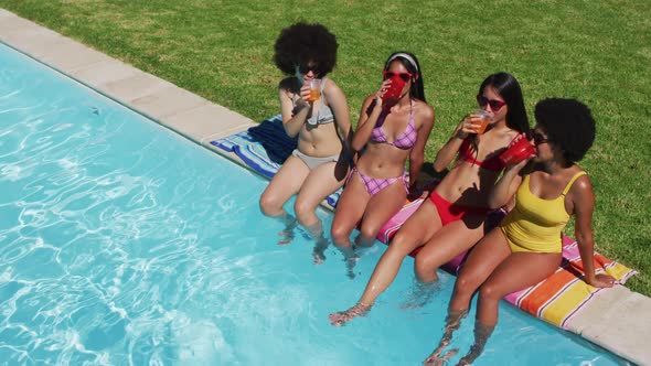 Group of diverse girls enjoying their drinks while sitting by the pool