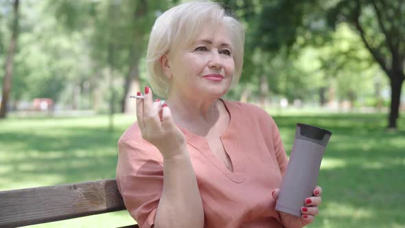 Relaxed Senior Woman Smoking in Sunny Park on Summer Day. Portrait of Carefree Caucasian Retiree