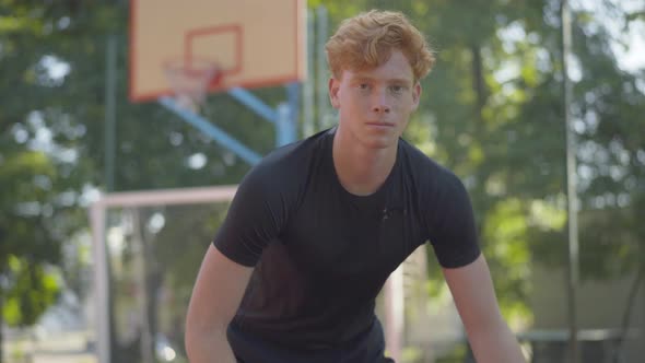 Portrait of Redhead Young Man Bouncing Ball and Looking at Camera. Confident Caucasian Basketball