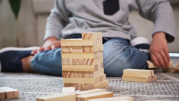 Child Builds a Wooden Tower for Playing Jenga Sitting on the Floor at Home