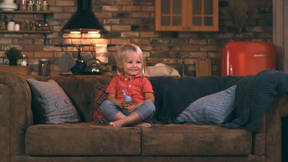 Little Boy at the Age of Three, Sitting on a Sofa with a Toy and Smiling Cute, Looking To the Side