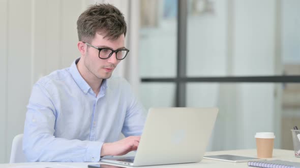 Attractive Young Man Looking at Camera While Using Laptop in Office