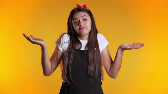 Young Unsure Woman in Dress Shrugs Her Arms, Makes Gesture of I Don't Know, Care