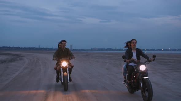 Cinematic Shot of Two Young Couples Riding on Vintage Motorcycles After Sunset on Beach Slow Motion