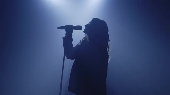 Backlit Silhouette of Singer Vocalist Girl Standing in Dark Nightclub Disco Studio and Start Singing