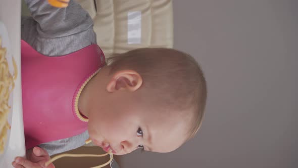 Toddler eats spaghetti for dinner while sitting on a feeding chair