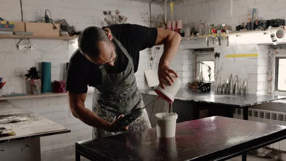 A male handyman mixes paint in a can in a workshop. A sculptor mixes resin with paint to a vase.