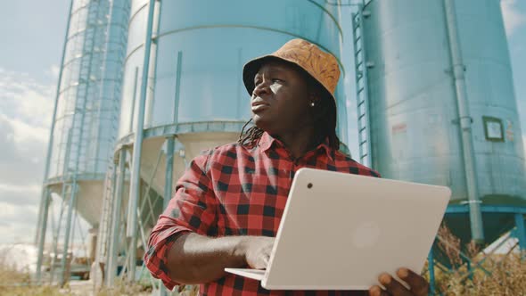 African Farmer Using Laptop in Front of the Silo Storage System