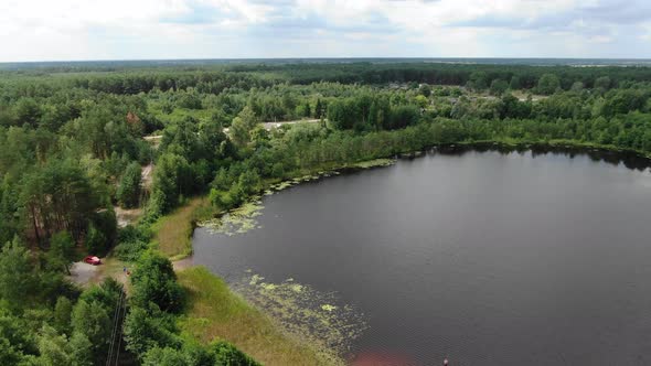 Aerial View of Small Lake Tracking Backward Revealing Thick Forestry