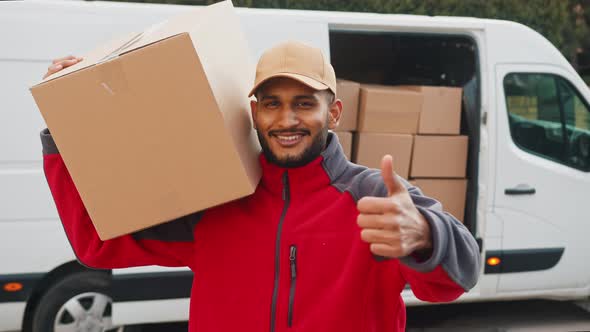 Delivery Boy Carrying A Cardboard Box On His Shoulder Making Thumbs Up Sign
